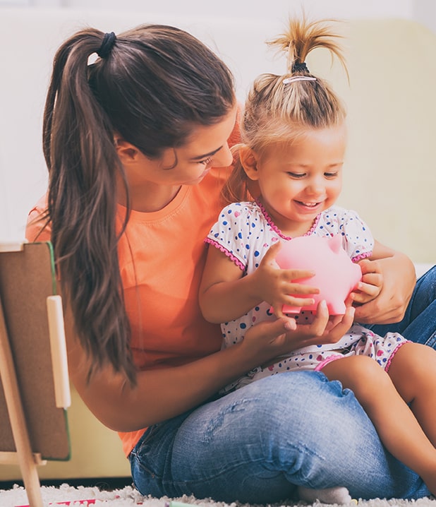 mother and daughter smiling while the daughter holds a piggybank