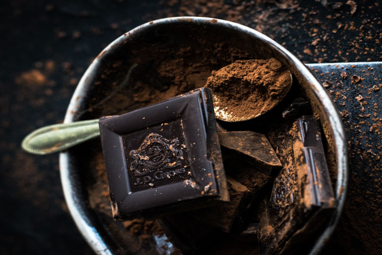 Aerial view of squares of dark chocolate with cocoa dust in a cup with a silver spoon