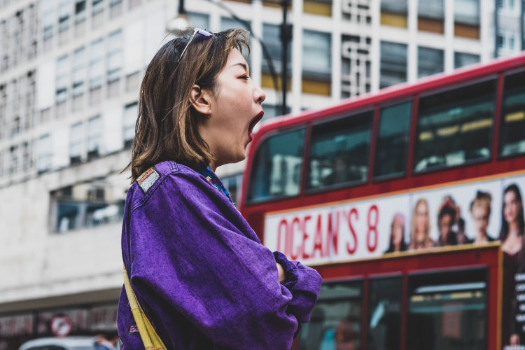 A brunette woman wearing a purple jacket yawns due to daytime sleepiness from sleep apnea