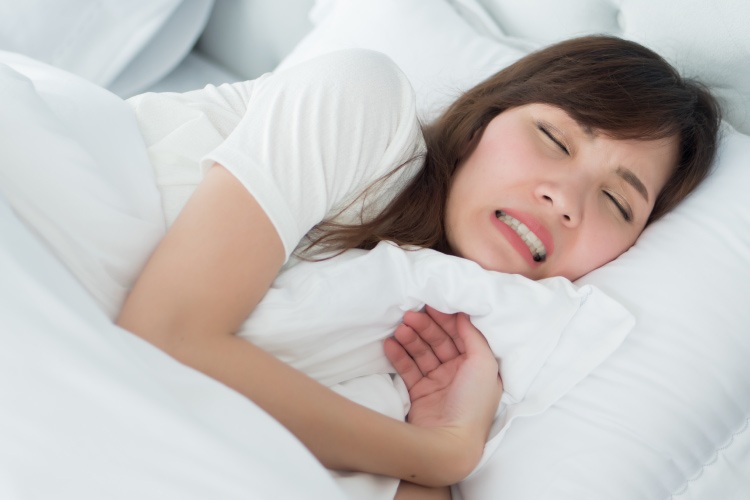 Brunette woman grinding her teeth as she sleeps on a white bed