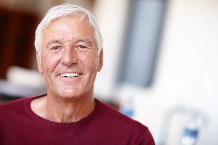 Older man with white hair and dentures smiles while wearing a red shirt