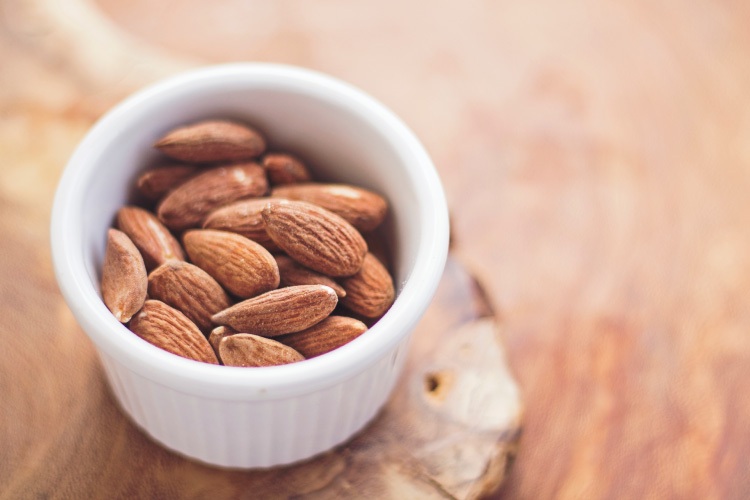 Aerial view of almonds in a white dish on a wooden counter, one of the many foods good for teeth