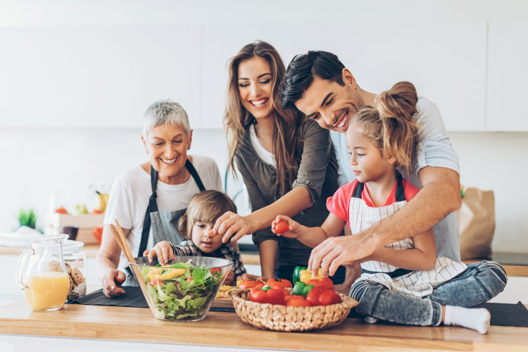 A mom and dad make a healthy dinner in the kitchen with their 2 kids and Gramma