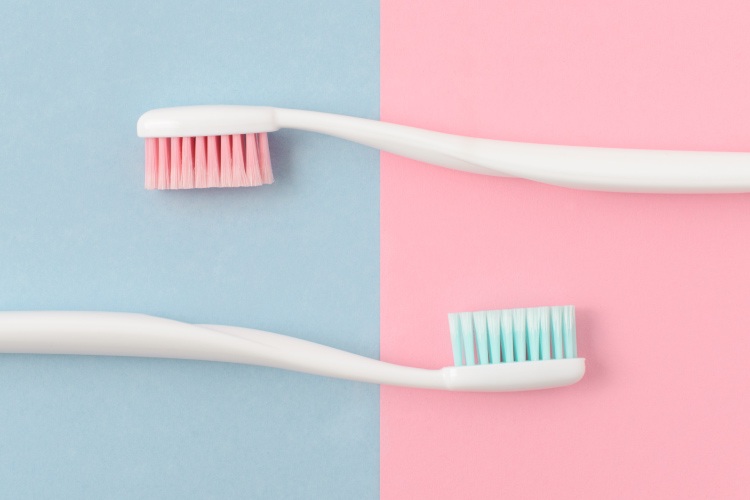 Aerial view of two toothbrushes against a split purple and pink background that need toothpaste
