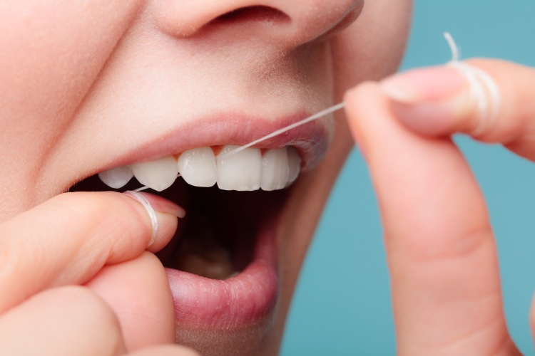 Closeup of a woman's mouth as she threads floss through her front teeth