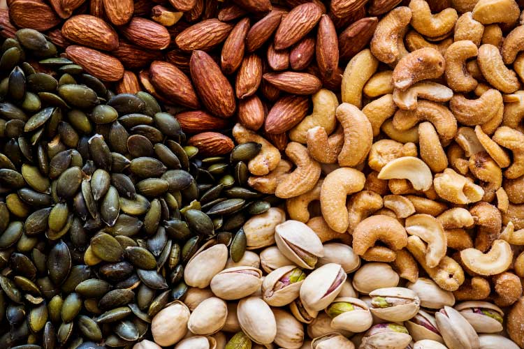 Aerial view of cashews, pistachios, almonds, and pumpkin seeds divided into 4 touching piles