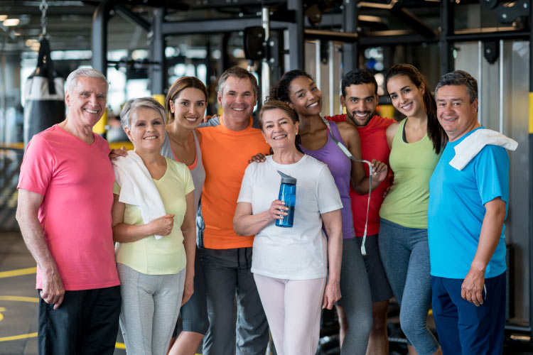 Group of people of mixed ages smile in workout clothes after exercising at the gym