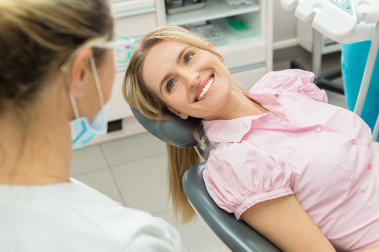 Blonde woman in a pink shirt smile after dental surgery in a dental chair