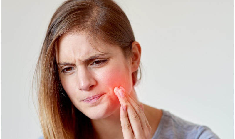 Young woman with toothache indicated by a glowing red spot on her cheek and pained look