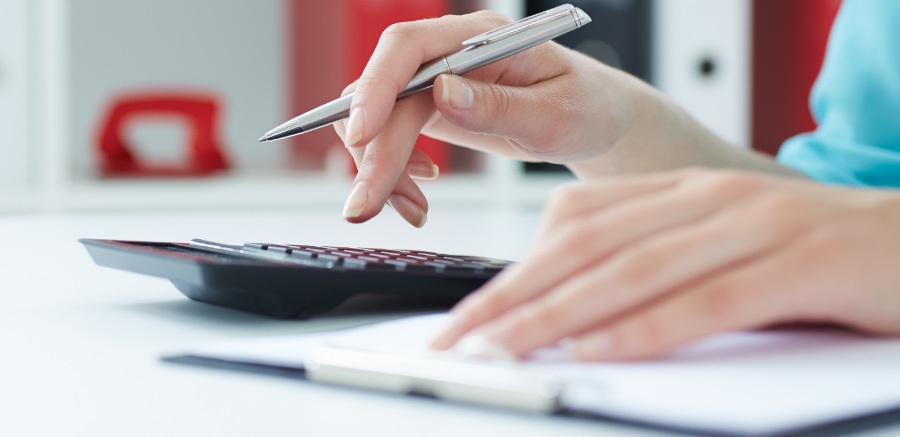 Hands holding a pen and working a calculator next to a note pad to determine dental finances