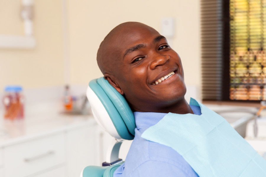 Smiling young Black man in the dental chair while getting a composite tooth filling 