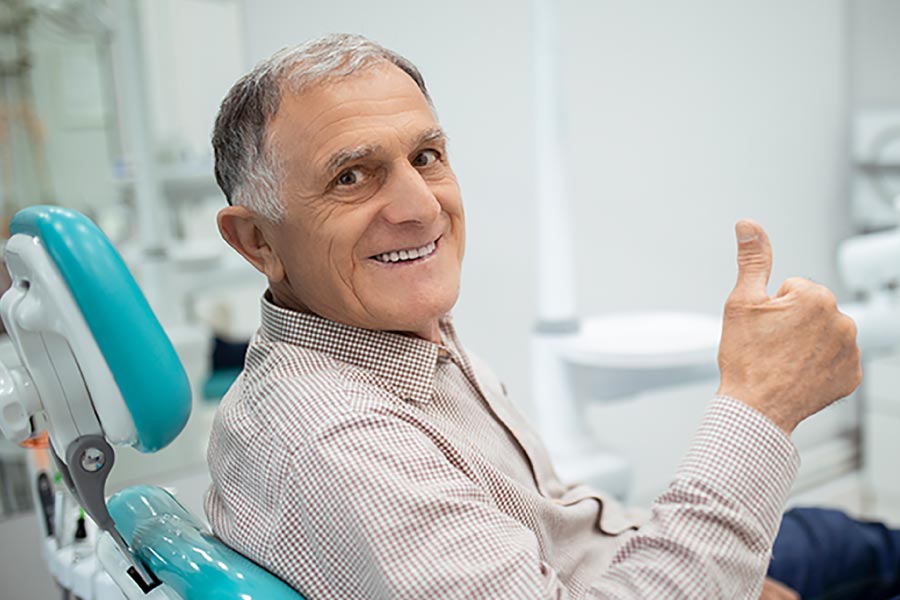 Mature man giving the thumbs up sign in the dental chair awaiting a bone graft