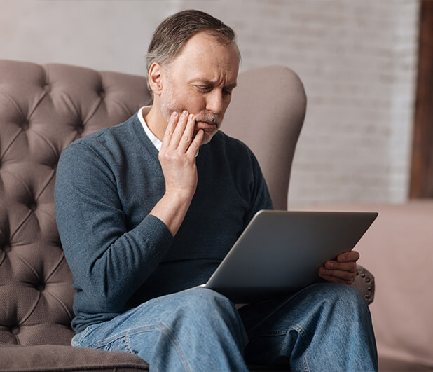 man holding his jaw in pain while looking at his laptop