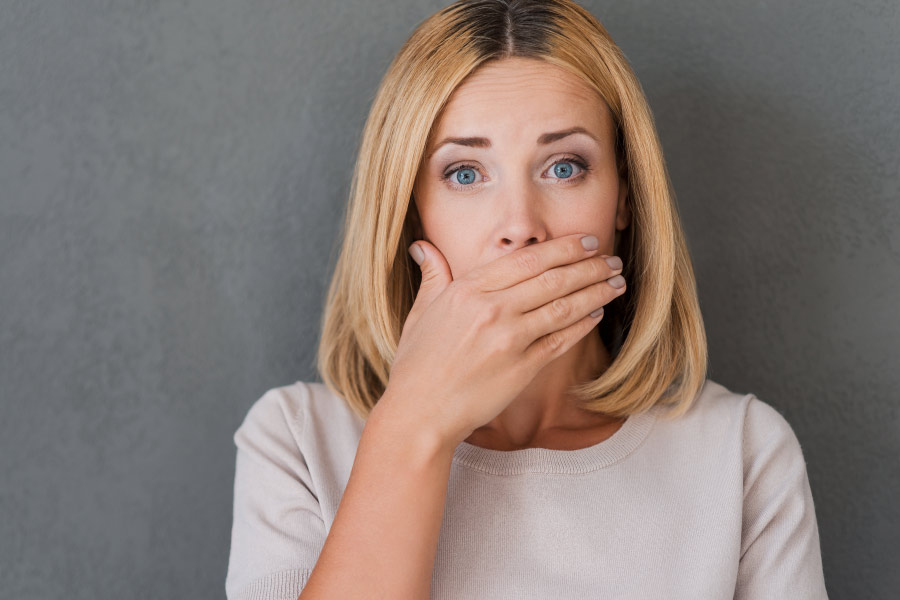 Blond woman covering her mouth because she's worried about bad breath.