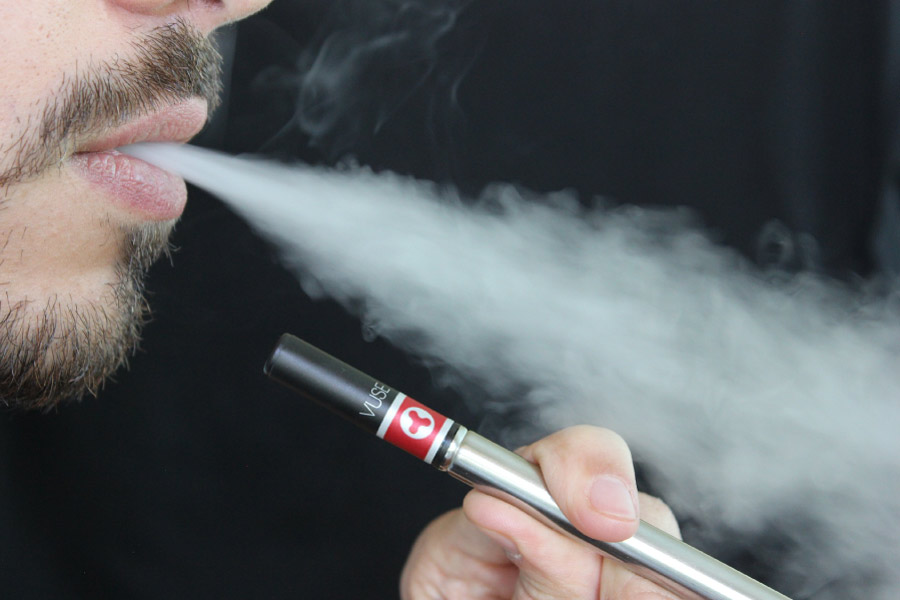 Photo showing just a man's chin and mouth as he expels smoke while holding an e-cigarette.