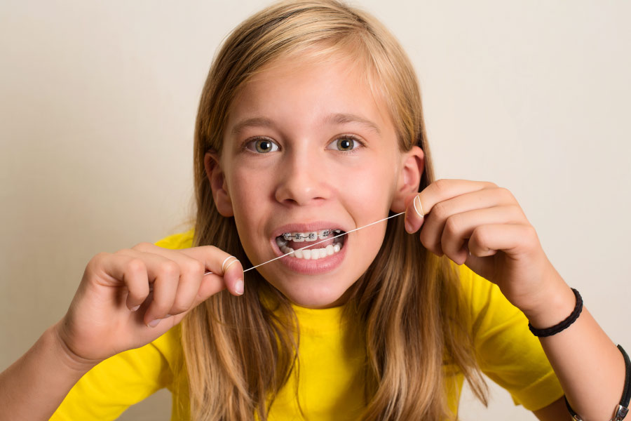 Young teen flossing her braces.