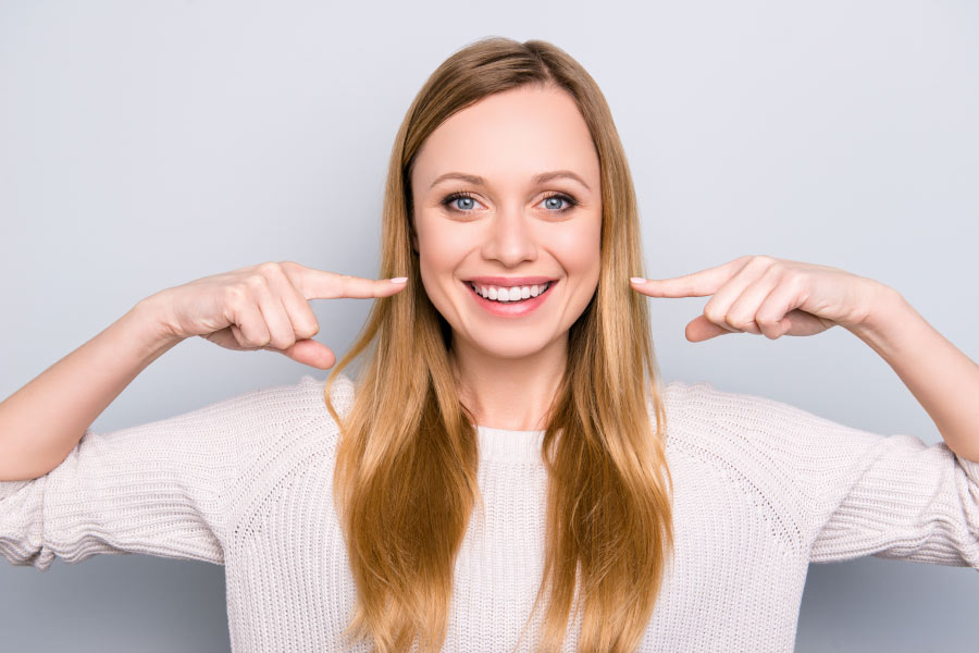 Young woman pointing to her bright white smile.