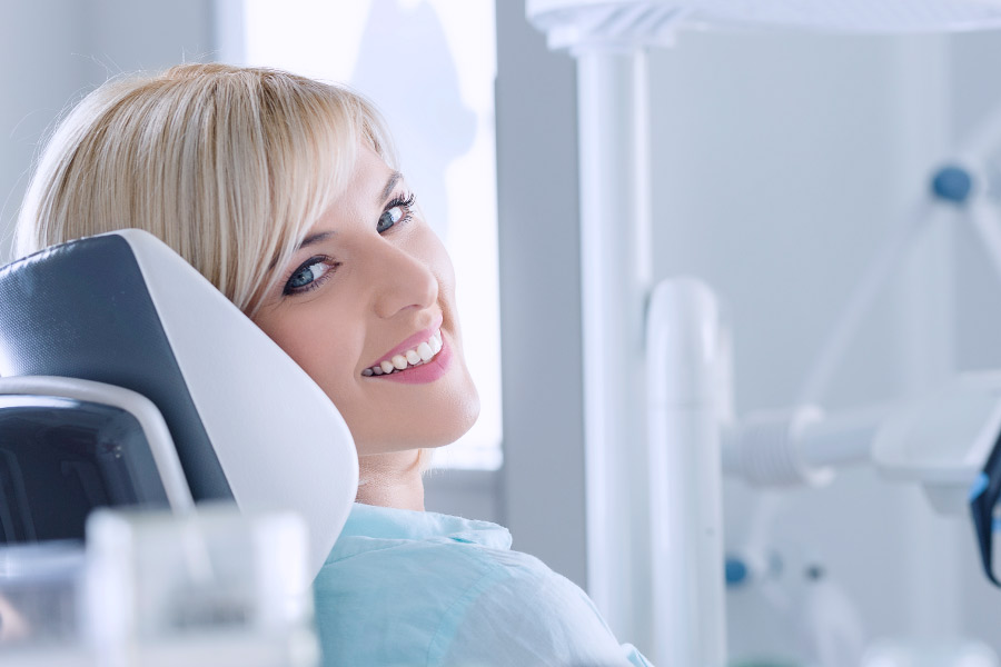 Smiling blond woman in dental chair for an exam and cleaning.