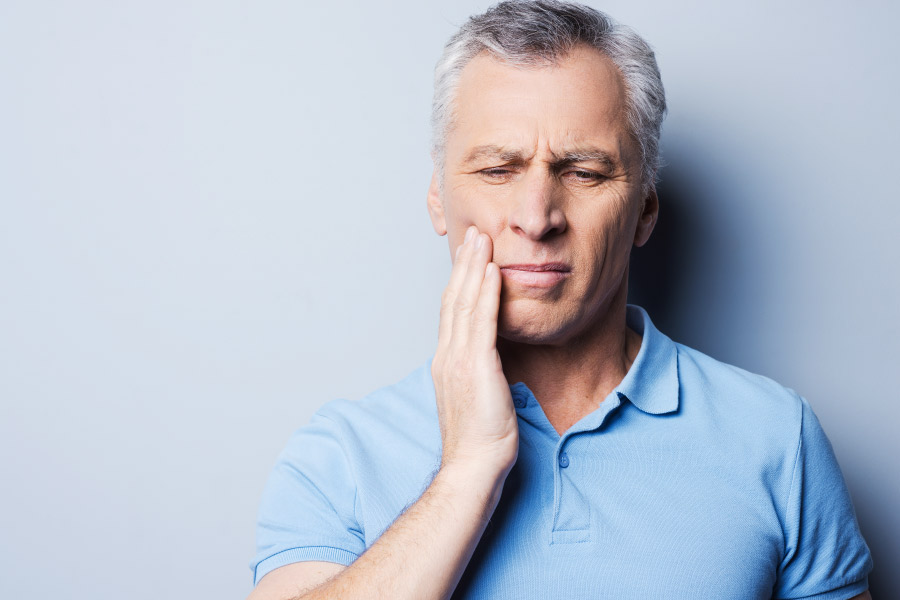 Gray haired man holding his cheek due to tooth pain caused by sensitivity.