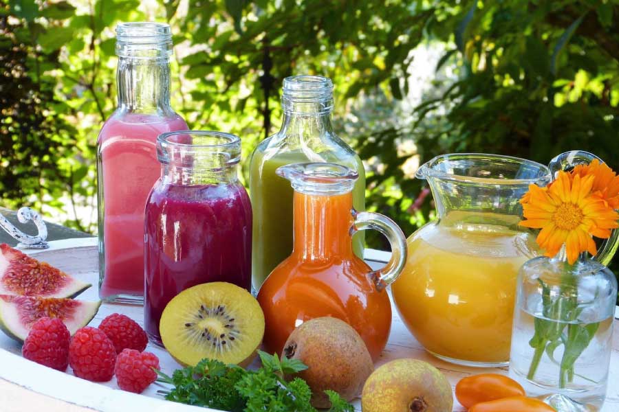 Fruit and vegetable smoothies arranged on a tray with cut fruit on a tables outside.