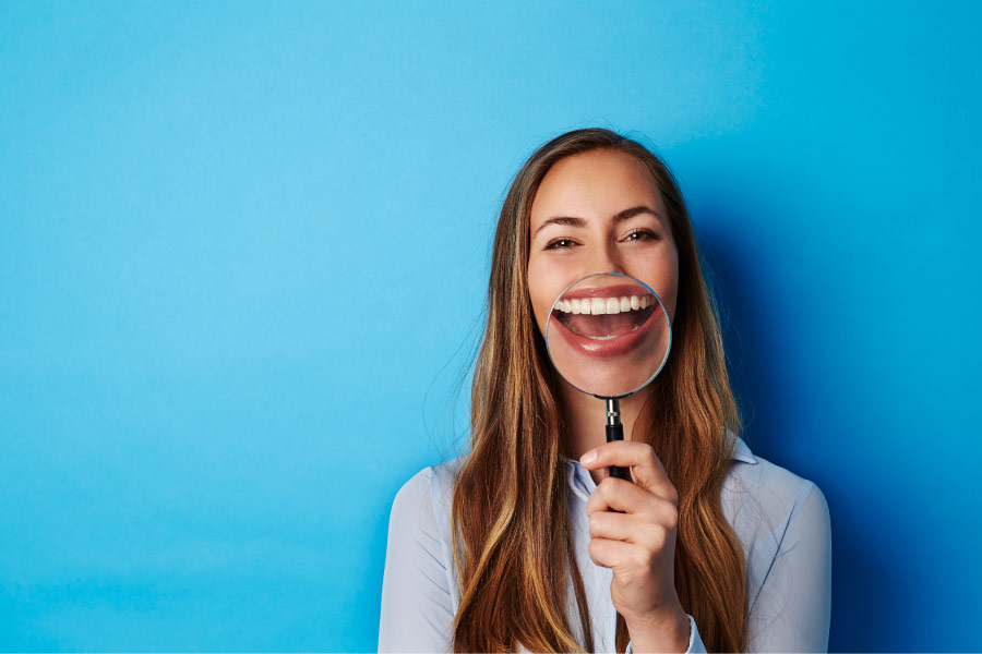 Smiling woman with a magnifying glass enlarging her beautiful smile.