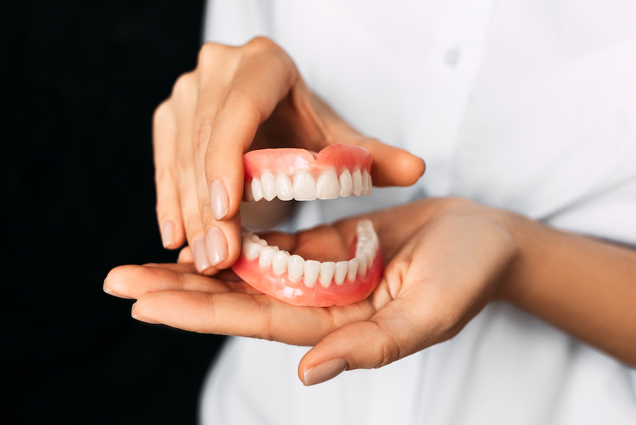 A dentist is holding dentures in his hands. Dental prosthesis in the hands of the doctor close-up. Front view of complete denture. Dentistry conceptual photo. Prosthetic dentistry. False teeth