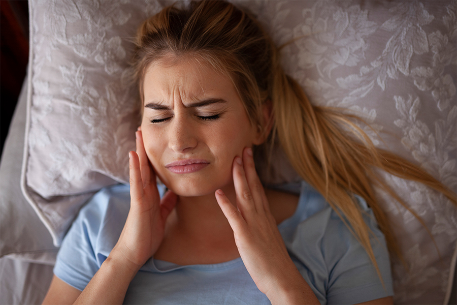Blonde haired woman with jaw pain caused by bruxism.